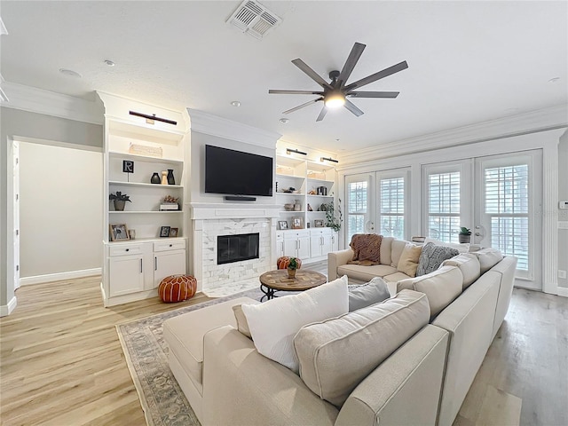 living room featuring a high end fireplace, visible vents, light wood-style flooring, and ornamental molding