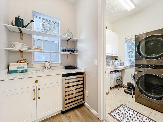 laundry area with wine cooler, stacked washer and clothes dryer, cabinet space, a textured ceiling, and baseboards