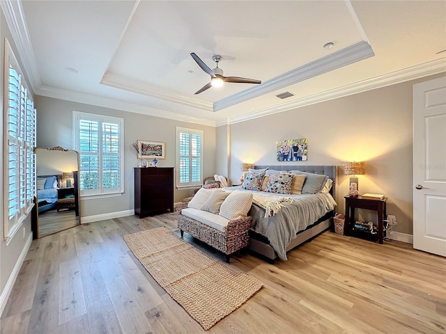 bedroom featuring light wood-style floors, visible vents, a tray ceiling, and baseboards