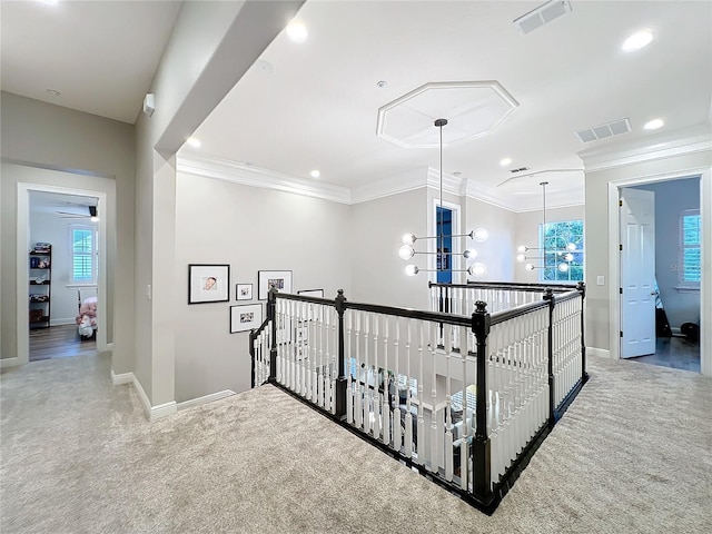 hallway with carpet, visible vents, ornamental molding, and an upstairs landing