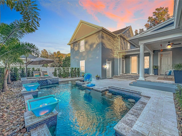 pool at dusk with a patio, fence, and a pool with connected hot tub