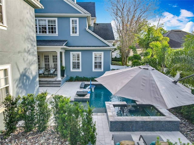 back of property with french doors, stucco siding, an outdoor pool, and an in ground hot tub