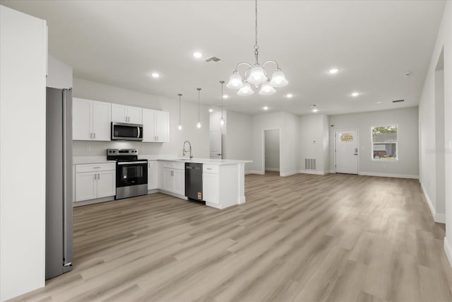 kitchen with light wood finished floors, stainless steel appliances, open floor plan, a sink, and a peninsula