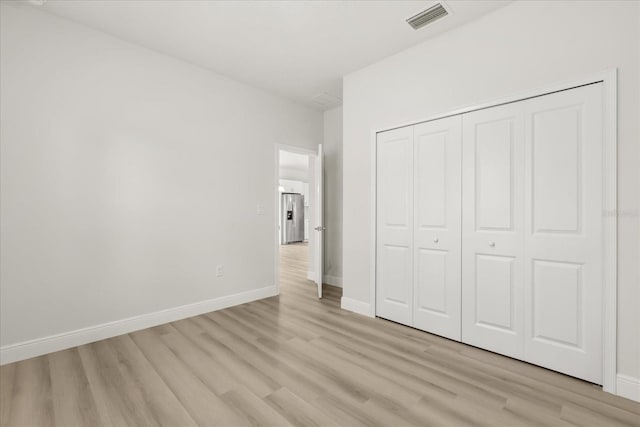 unfurnished bedroom featuring baseboards, stainless steel fridge, visible vents, and light wood-style floors