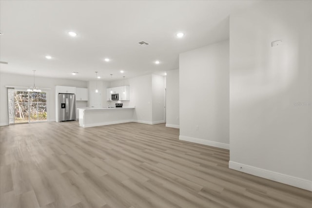 unfurnished living room with light wood-style flooring, a notable chandelier, recessed lighting, visible vents, and baseboards