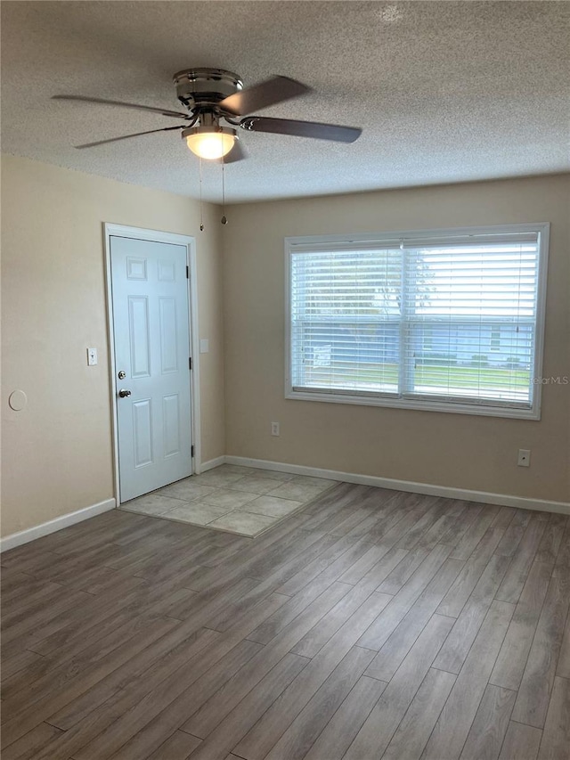 spare room with light wood finished floors, baseboards, and a textured ceiling