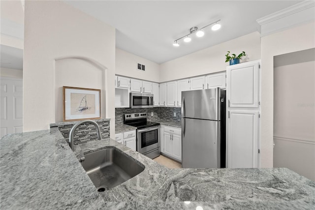 kitchen featuring light stone counters, tasteful backsplash, appliances with stainless steel finishes, white cabinets, and a sink