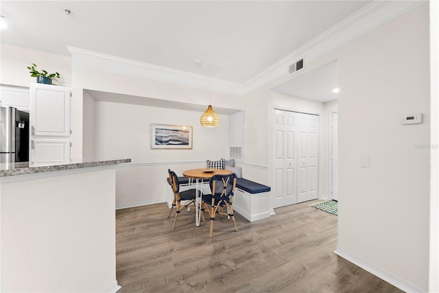 dining room with baseboards, light wood finished floors, visible vents, and crown molding