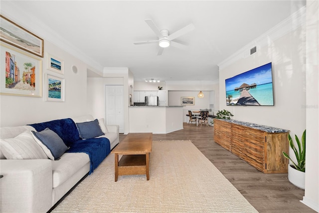 living area with ceiling fan, visible vents, crown molding, and wood finished floors