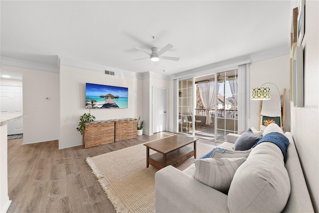 living room with crown molding, visible vents, light wood-style floors, a ceiling fan, and baseboards