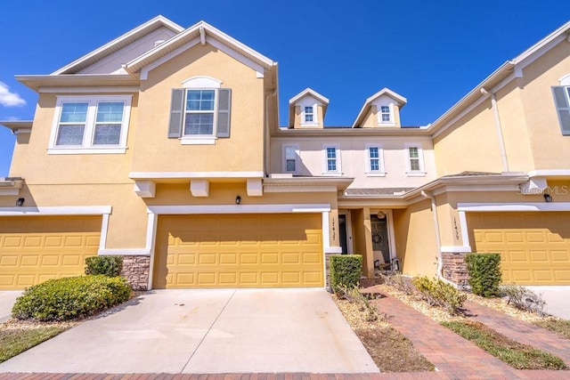 townhome / multi-family property featuring driveway, stone siding, an attached garage, and stucco siding