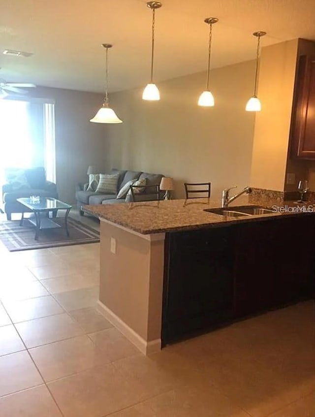 kitchen featuring light tile patterned flooring, a sink, open floor plan, hanging light fixtures, and light stone countertops