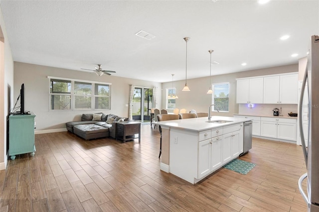 kitchen featuring a center island with sink, light countertops, open floor plan, white cabinets, and a sink