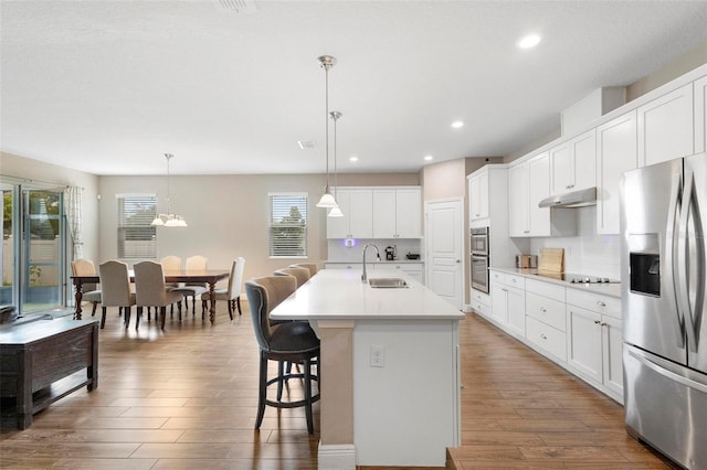 kitchen with a center island with sink, appliances with stainless steel finishes, light countertops, pendant lighting, and a sink