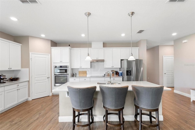 kitchen with appliances with stainless steel finishes, hanging light fixtures, a kitchen island with sink, light countertops, and a sink