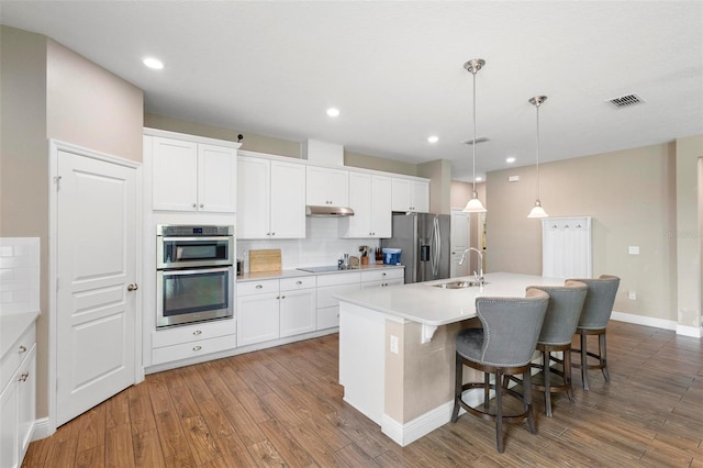 kitchen with appliances with stainless steel finishes, decorative light fixtures, a kitchen island with sink, white cabinetry, and a sink