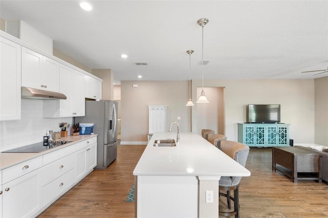 kitchen with a center island with sink, a breakfast bar area, black electric stovetop, under cabinet range hood, and a sink