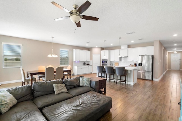 living room with baseboards, a textured ceiling, visible vents, and wood finished floors