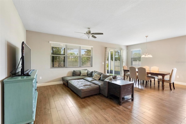 living area featuring ceiling fan with notable chandelier, a textured ceiling, baseboards, and wood finished floors