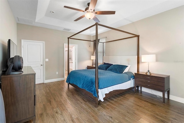 bedroom featuring dark wood-style flooring, visible vents, a raised ceiling, and baseboards