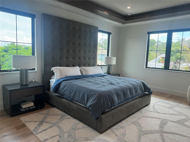 bedroom featuring light wood-type flooring, a tray ceiling, baseboards, and recessed lighting