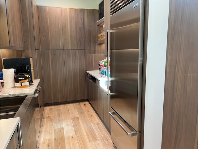 kitchen with open shelves, high end fridge, modern cabinets, light wood-style flooring, and light stone countertops