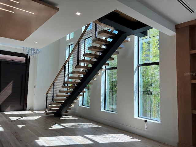 staircase with a healthy amount of sunlight, wood finished floors, and visible vents