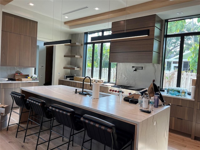 kitchen with backsplash, a kitchen island with sink, modern cabinets, light wood finished floors, and a sink