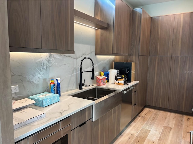 kitchen with light wood-type flooring, light stone counters, stainless steel dishwasher, and modern cabinets
