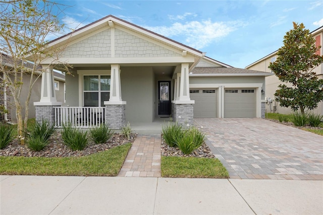 craftsman house with covered porch, decorative driveway, an attached garage, and stucco siding