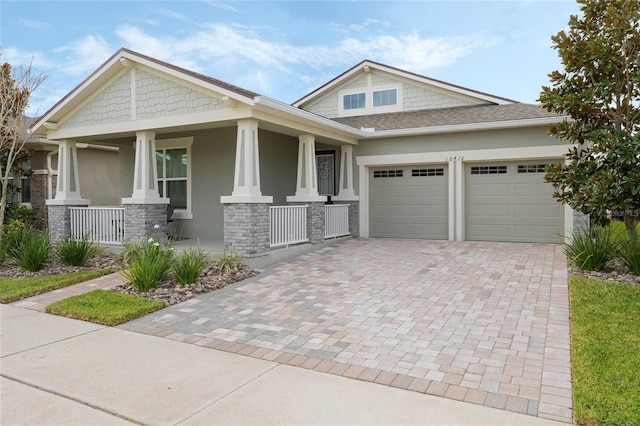 craftsman inspired home with a garage, covered porch, stone siding, decorative driveway, and stucco siding