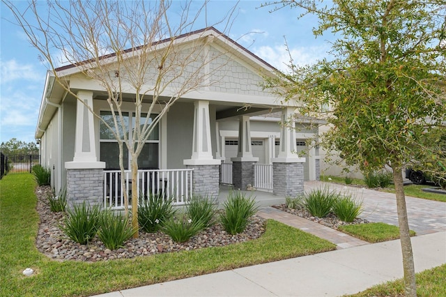 view of front facade with decorative driveway, covered porch, stone siding, and stucco siding