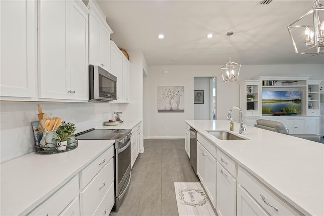 kitchen with white cabinets, hanging light fixtures, stainless steel appliances, light countertops, and a sink