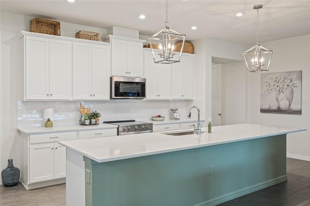 kitchen with a center island with sink, stainless steel appliances, light countertops, hanging light fixtures, and a sink