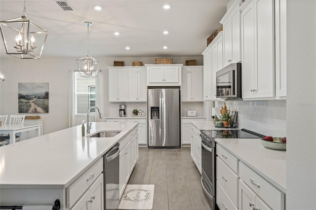 kitchen featuring a center island with sink, decorative light fixtures, stainless steel appliances, light countertops, and a sink