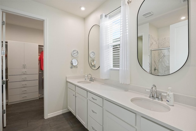 full bath with double vanity, a stall shower, a sink, and a walk in closet