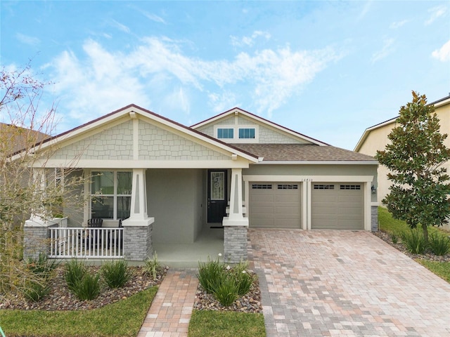 craftsman inspired home featuring an attached garage, a porch, decorative driveway, and stucco siding