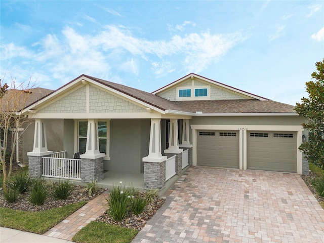 craftsman house with decorative driveway, stucco siding, a porch, an attached garage, and stone siding