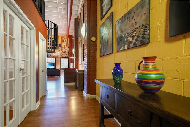 corridor with french doors, wood finished floors, concrete block wall, and baseboards