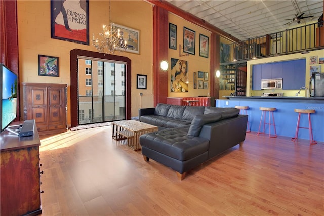 living room featuring light wood-type flooring, a towering ceiling, and ceiling fan with notable chandelier