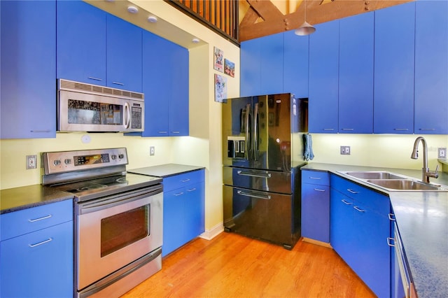 kitchen with dark countertops, blue cabinetry, appliances with stainless steel finishes, and a sink