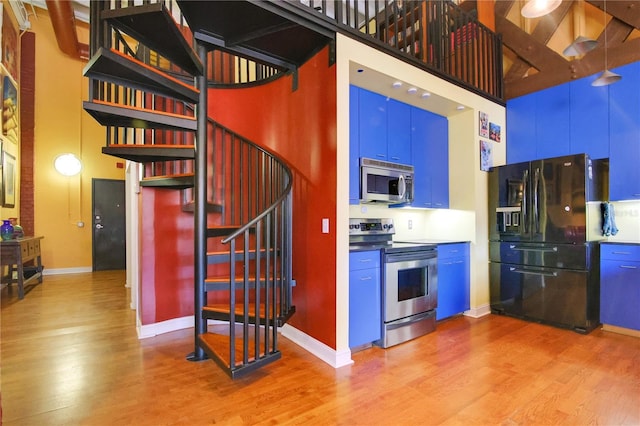 kitchen with light wood-style flooring, a high ceiling, baseboards, and stainless steel appliances