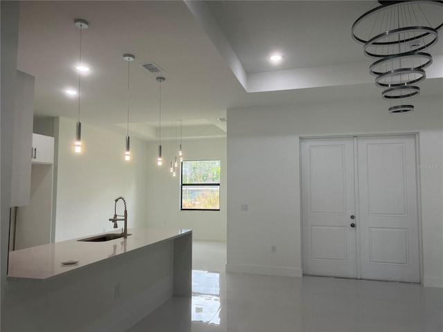 kitchen with recessed lighting, a sink, white cabinets, a raised ceiling, and decorative light fixtures