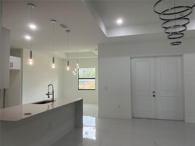 kitchen featuring visible vents, a sink, decorative light fixtures, and white cabinetry