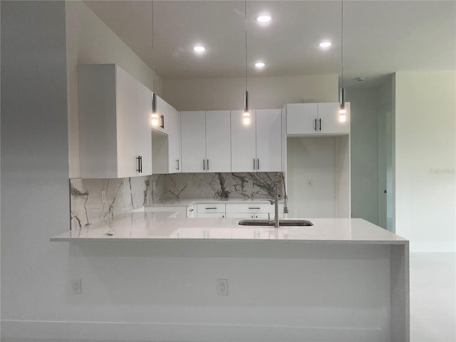 kitchen featuring hanging light fixtures, a peninsula, white cabinetry, and a sink