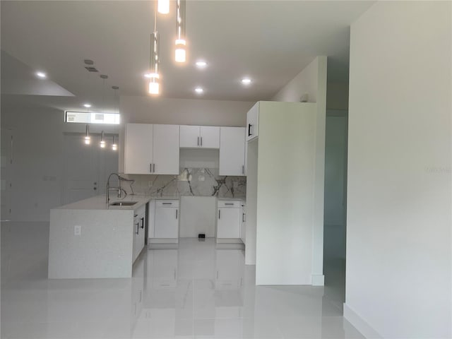 kitchen with marble finish floor, hanging light fixtures, backsplash, white cabinets, and a sink