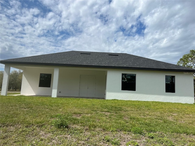 back of property featuring roof with shingles, a yard, and stucco siding