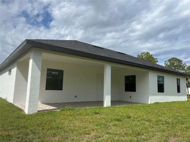 rear view of property featuring a yard, roof with shingles, stucco siding, and a patio