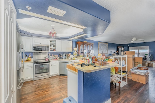 kitchen featuring stainless steel appliances, a raised ceiling, light countertops, white cabinetry, and a peninsula