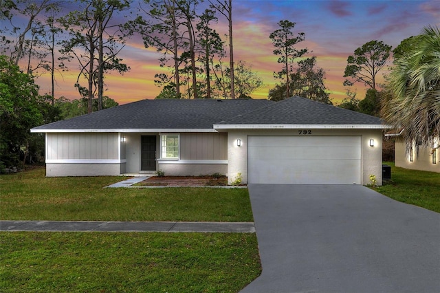 ranch-style home featuring a garage, a shingled roof, a lawn, concrete driveway, and stucco siding